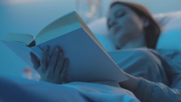 Paciente feminina deitada em uma cama de hospital e lendo um livro — Vídeo de Stock