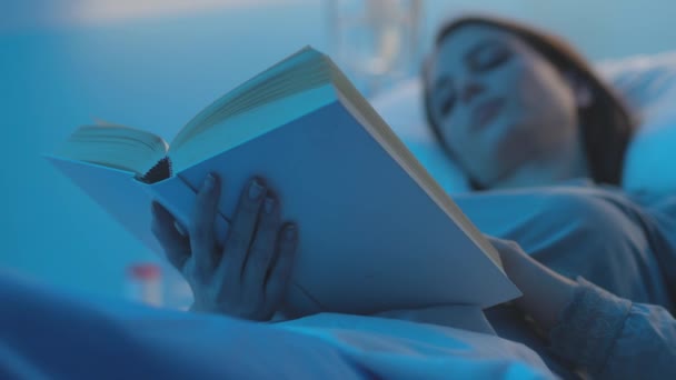 Női beteg fekszik egy kórházi ágyban, és könyvet olvas. — Stock videók