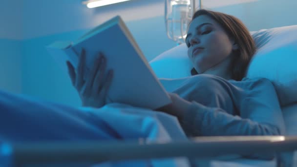 Γυναίκα ασθενής ξαπλωμένη στο κρεβάτι του νοσοκομείου και διαβάζοντας ένα βιβλίο — Αρχείο Βίντεο