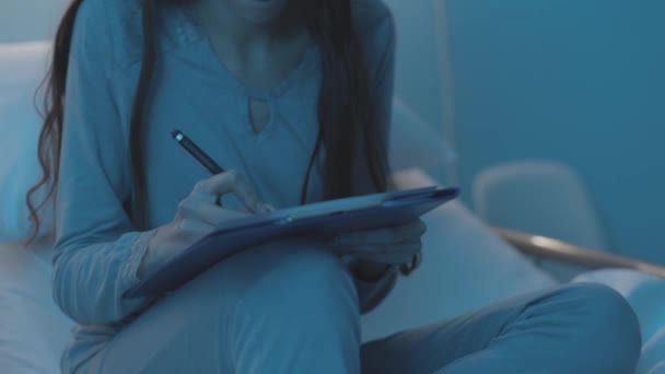 Jeune patient assis sur un lit d'hôpital et remplissant un formulaire médical — Video