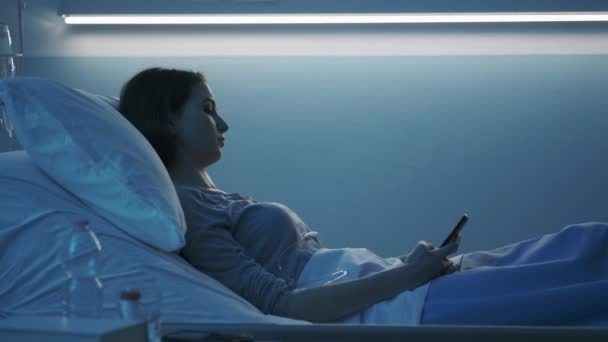 Jeune patiente couchée au lit à l'hôpital et utilisant son smartphone — Video