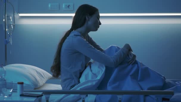 Jonge patiënt die 's nachts op een ziekenhuisbed zit en zich verdrietig voelt — Stockvideo