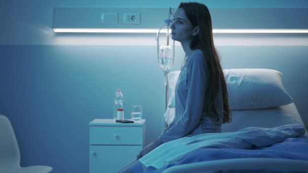 Young patient sitting on a hospital bed at night and feeling sad — Stock Video