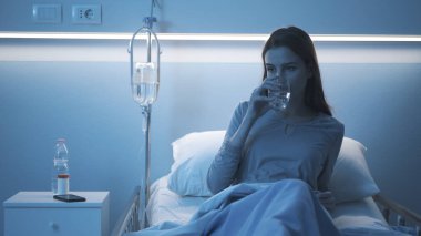 Hastanedeki hasta yatakta yatıp su içiyor.