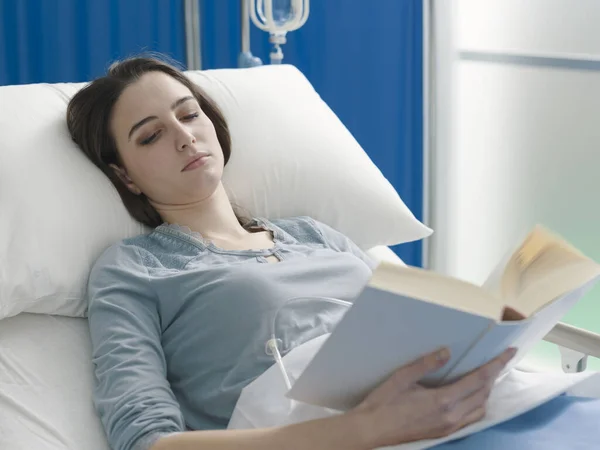 Pasien muda berbaring di ranjang rumah sakit dan membaca buku — Stok Foto
