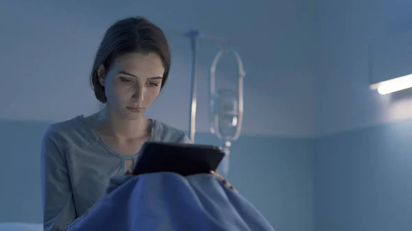 Hastanede genç uykusuz bir hasta tabletle bağlantı kuruyor. — Stok fotoğraf