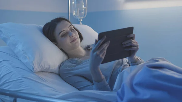 Jonge lachende patiënt liggend in bed en verbonden met een tablet — Stockfoto