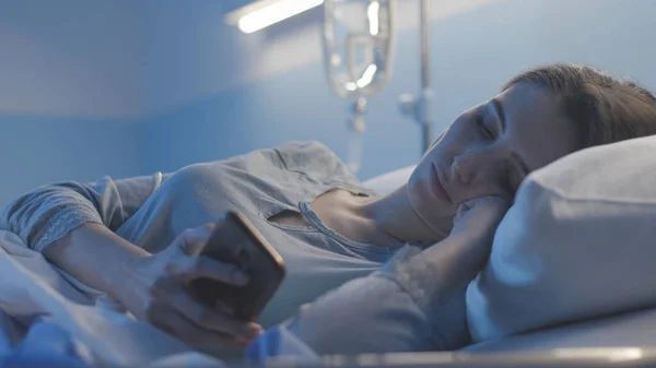 Uykusuz hasta yatakta uzanıyor ve akıllı telefonuyla sohbet ediyor. — Stok fotoğraf