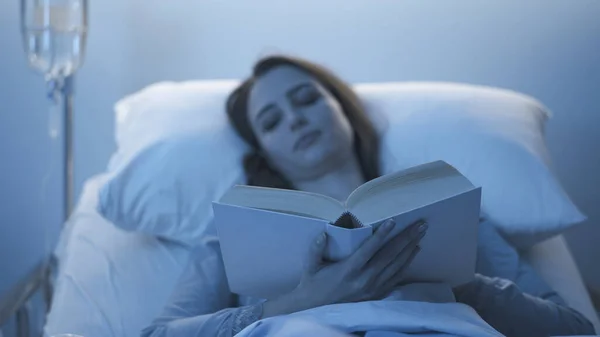 Νεαρός άγρυπνος ασθενής ξαπλωμένος στο κρεβάτι του νοσοκομείου και διαβάζοντας — Φωτογραφία Αρχείου