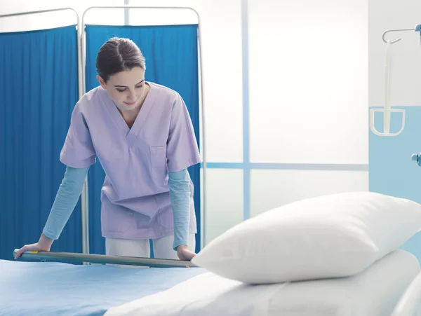 Νεαρή εκπαιδευόμενη νοσοκόμα που εργάζεται στο νοσοκομείο και προσαρμόζει το κρεβάτι — Φωτογραφία Αρχείου