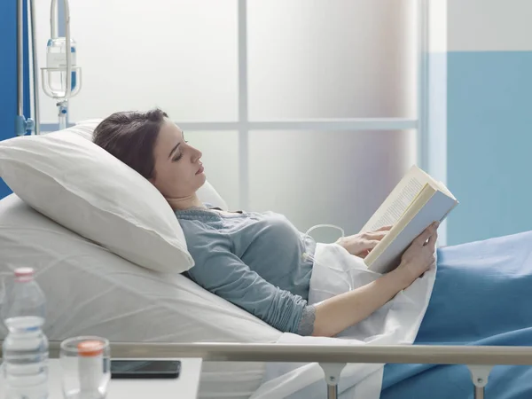 Junge Patientin liegt im Krankenhausbett und liest ein Buch — Stockfoto