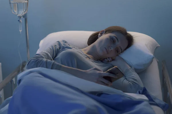Paciente insomne acostada en la cama y charlando con su smartphone — Foto de Stock