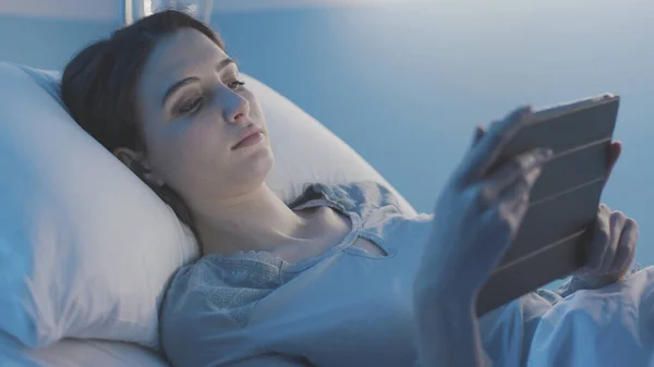 Молодой пациент лежит в постели и подключается к планшету ночью — стоковое фото
