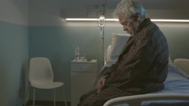 Hastane yatağında oturan uykusuz yaşlı adam.