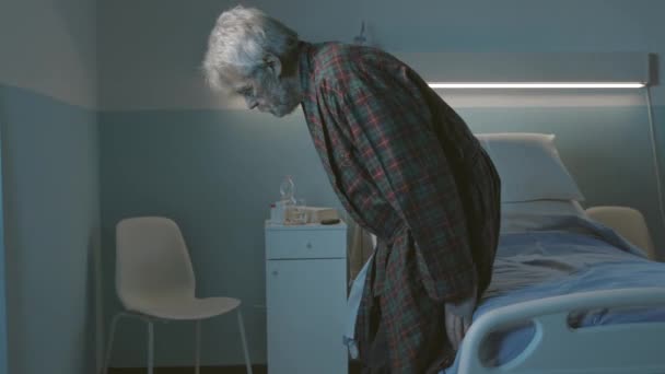 Sad lonely elderly man sitting on a hospital bed at night — Stock Video