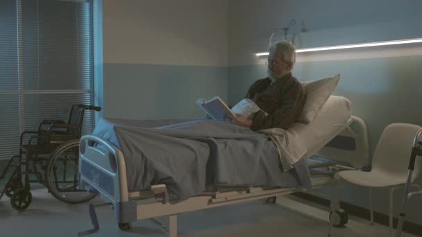 Sleepless senior man in het ziekenhuis het lezen van een boek — Stockvideo