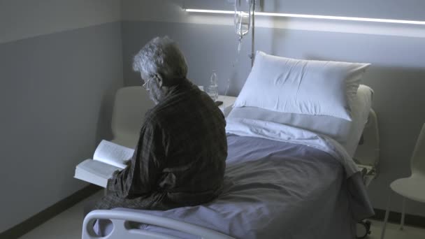 Бессонный пожилой человек в больнице читает книгу — стоковое видео