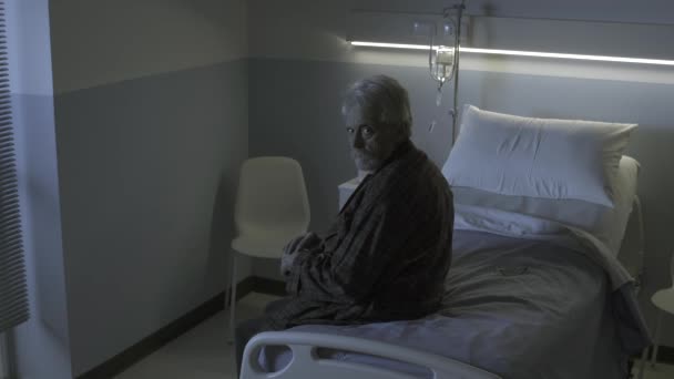 Старший чоловік в лікарні прикриває камеру, яка спостерігає за ним — стокове відео