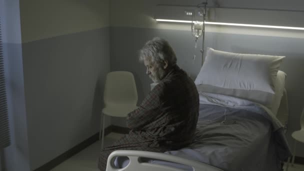 Грустный одинокий пожилой человек, сидящий на больничной койке ночью — стоковое видео