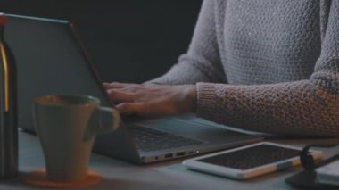 Masasında oturmuş laptopuyla yazı yazan bir kadın.