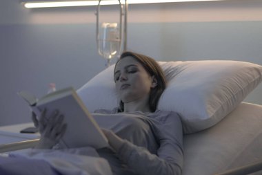 Genç, uykusuz bir hasta gece hastane yatağında uzanıp kitap okuyor.