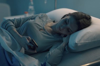 Uykusuz endişeli hasta gece geç saatte hastanede yatıp akıllı telefonuyla sohbet ediyor.