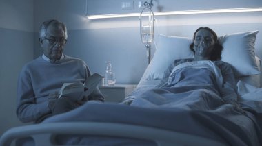 Hastanede kızının yanında oturan ve geceleri ona yardım eden kıdemli bir adam, bir kitap okuyor ve onu kontrol ediyor.