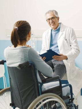 Kendine güvenen doktor, hastanede tekerlekli sandalyedeki belden aşağısı felçli hastayı ziyaret ediyor.
