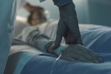 Doktor hastanede genç bir hastaya yardım ediyor ve nabzını ölçüyor. Yatakta uzanıyor ve uyuyor.