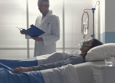 Profesyonel doktor hastanede yatan bir hastaya yardım ediyor. Tıbbi kayıtları kontrol ediyor.