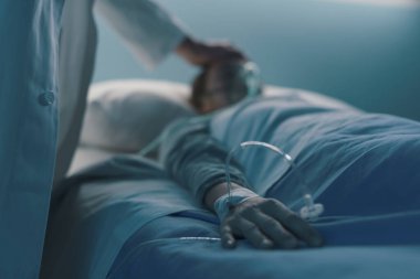 Hastanede yatan bir hasta gece yatağında yatıyor, bir doktor onunla ilgileniyor, elini kapat.
