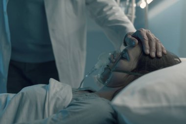 Hastanede yatan bir hasta gece yatarken, bir doktor onunla ilgileniyor ve alnına dokunuyor.