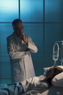 Profesyonel doktor geceleri hastasını kontrol ediyor, kadın yatakta uzanıyor ve oksijen maskesiyle uyuyor.