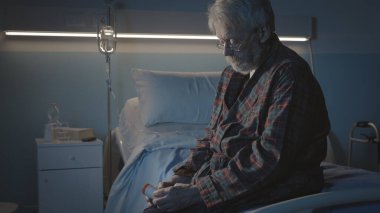 Geceleyin hastane yatağında tek başına oturan ve elinde ilaç şişesi tutan yaşlı bir adam uykusuzluk çekiyor ve depresyonda.