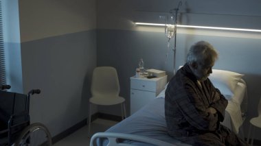 Bunalımlı son sınıf öğrencisi gece tek başına hastane yatağında oturuyor, kendini yalnız ve üzgün hissediyor.