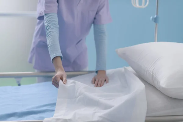 Expert young nurse working at the hospital, she is making the bed and changing sheets, healthcare service and assistance concept