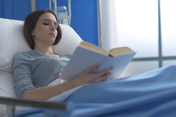 Χαλαρωμένη Νεαρή Γυναίκα Ξαπλωμένη Στο Κρεβάτι Του Νοσοκομείου Και Διαβάζοντας — Φωτογραφία Αρχείου