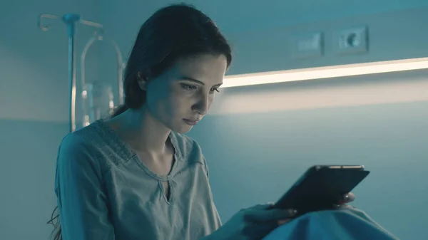 年轻的不眠症患者晚上躺在医院的病床上 她正在连接她的数码平板电脑 — 图库照片