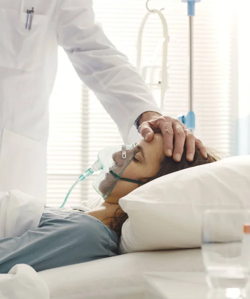 一位专业医生正在帮助一位躺在病床上的年轻病人 他正在触摸她的额头 他的保健理念 — 图库照片