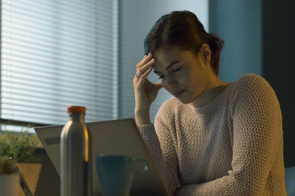 疲倦的年轻女人坐在办公桌前 用笔记本电脑工作 头疼得厉害 — 图库照片