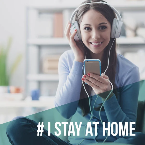 Akıllı telefonuyla müzik dinleyen ve gülümseyen bir kadın: Coronavirus önleme için sosyal medya kampanyasında evde kalıyorum