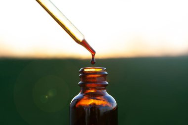 Dropper ve Kahverengi Cam Şişe. Kahverengi cam şişenin üzerinde aromaterapi esansından bir pipet damlası.