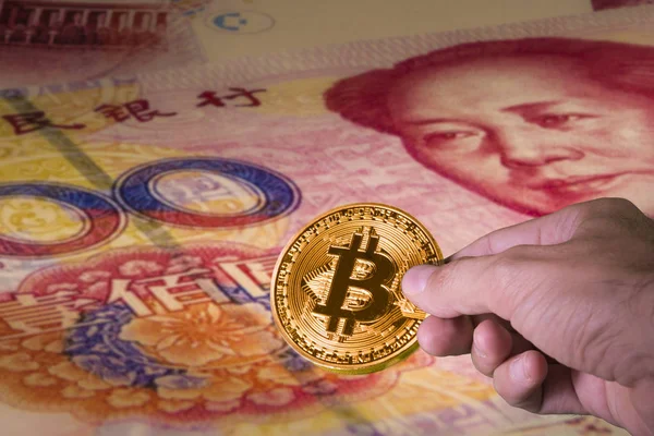 Bir bitcoin ve Çin Yuan faturaları arka planda tutan el