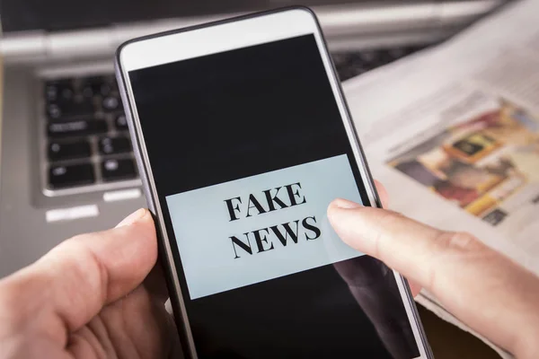 Mann hält ein Smartphone mit Fake-News-Wörtern auf dem Bildschirm. Fake News, Falschmeldung — Stockfoto