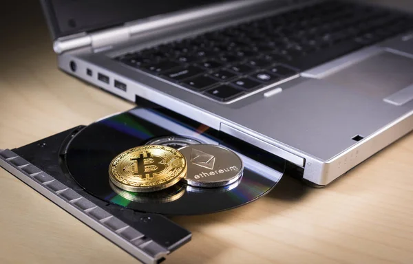Bitcoin e ethereum moedas sobre a unidade de CD de um laptop — Fotografia de Stock
