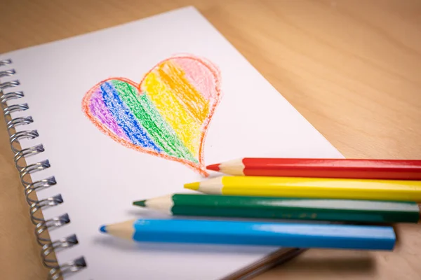 Corazón con los colores de la bandera LGTBI o GLBT en un cuaderno en blanco con bolígrafos arco iris — Foto de Stock