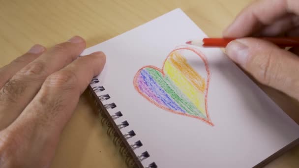 Coração com as cores da bandeira LGTBI ou GLBT em um caderno em branco com canetas de arco-íris — Vídeo de Stock