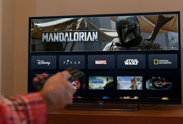 Barcelona, España. Noviembre 2019: El hombre tiene un control remoto con la nueva pantalla Disney plus en la TV — Foto de Stock