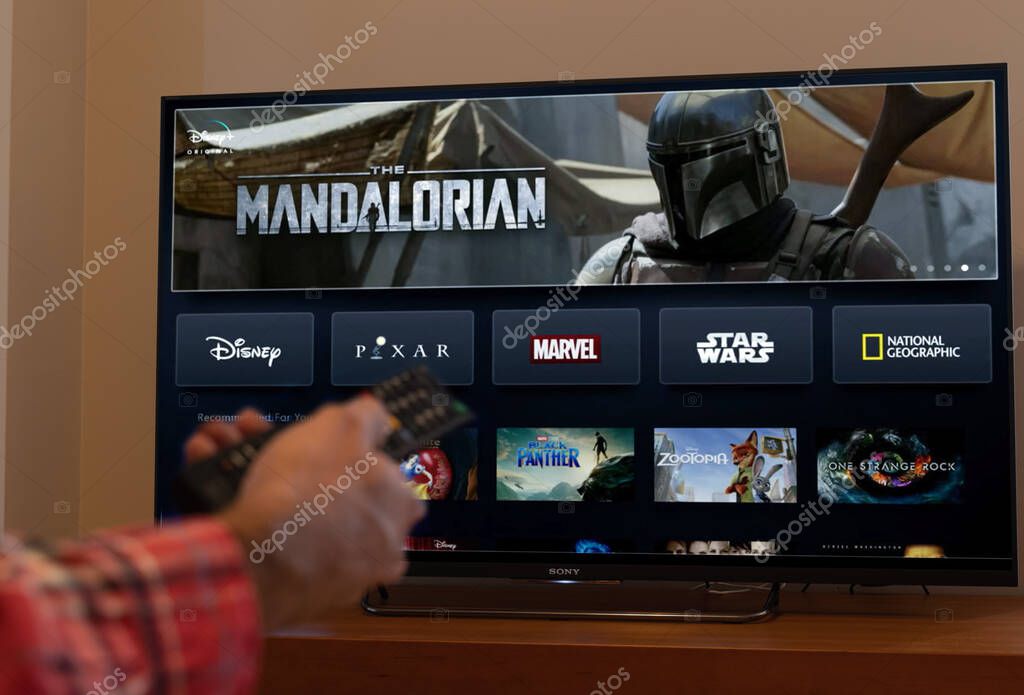 Barcelona, Spain. November 2019: Man holds a remote control With the new Disney plus screen on TV, showing The Mandalorian space western television series. .Illustrative editorial. Disney plus is an