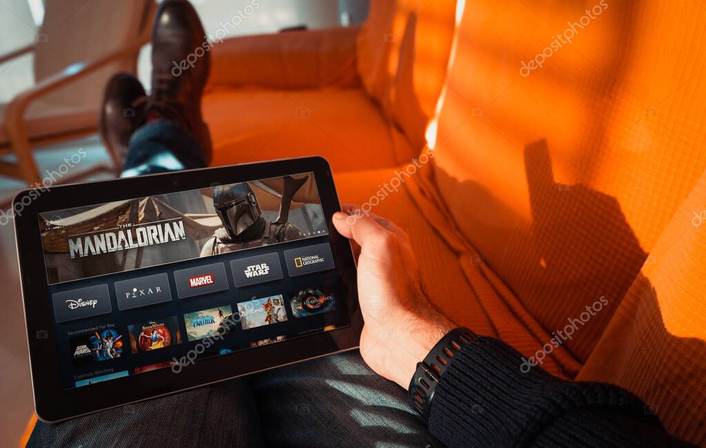 Barcelona, Spain. Jan 2019: Man holds a tablet with the new Disney plus on screen showing The Mandalorian space western television series. Illustrative editorial. Disney plus is an online video